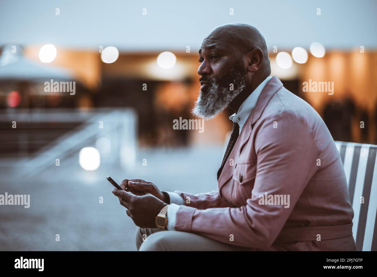 Une photo discrete d un homme noir chauve avec une barbe pleine de taille vetue d une veste rose pale semble pensive en etant assis et en tenant son telephone Photo Stock Alamy