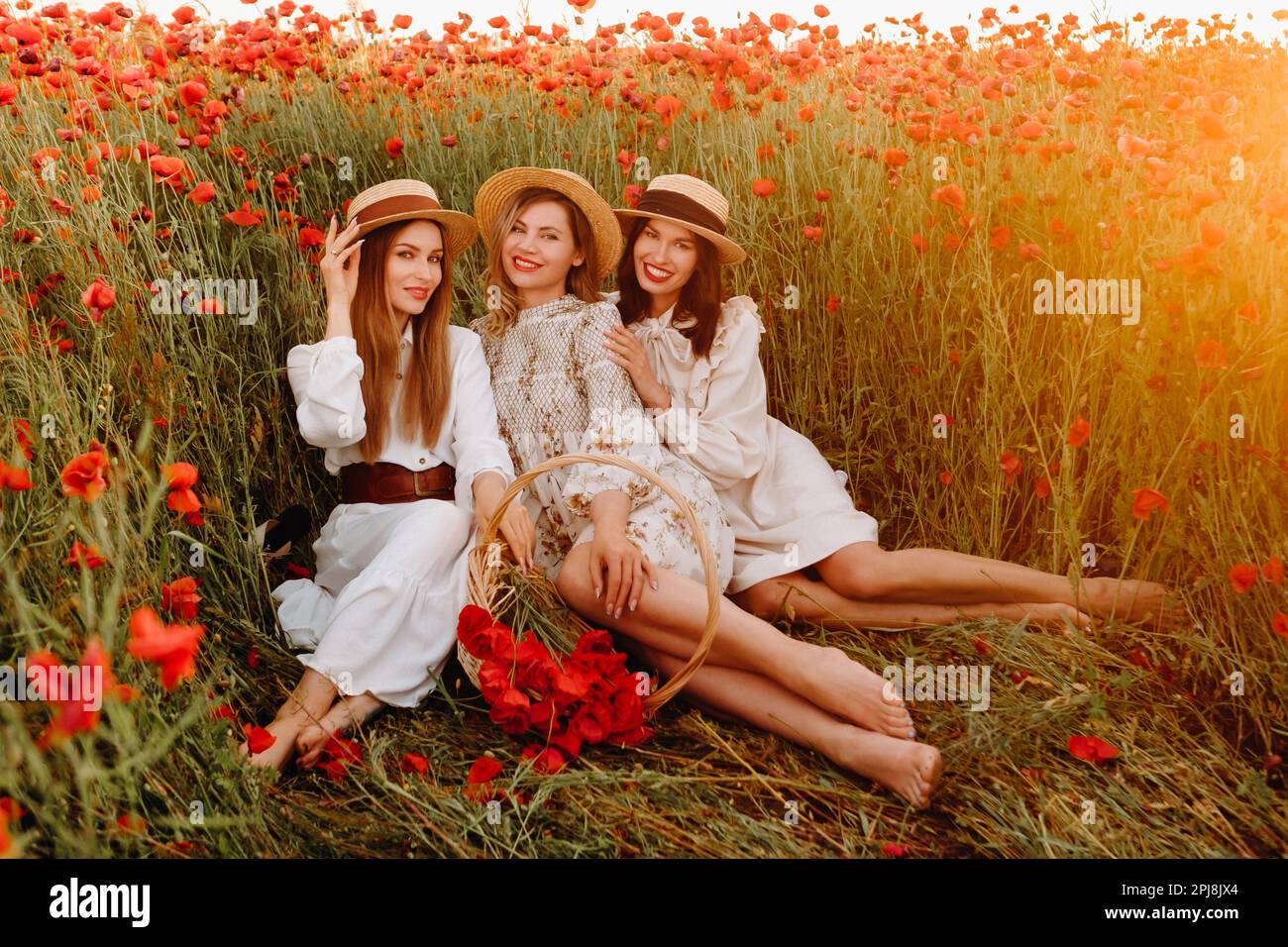 Drôles filles en robes et chapeaux dans un champ de pavot au coucher du soleil. Banque D'Images