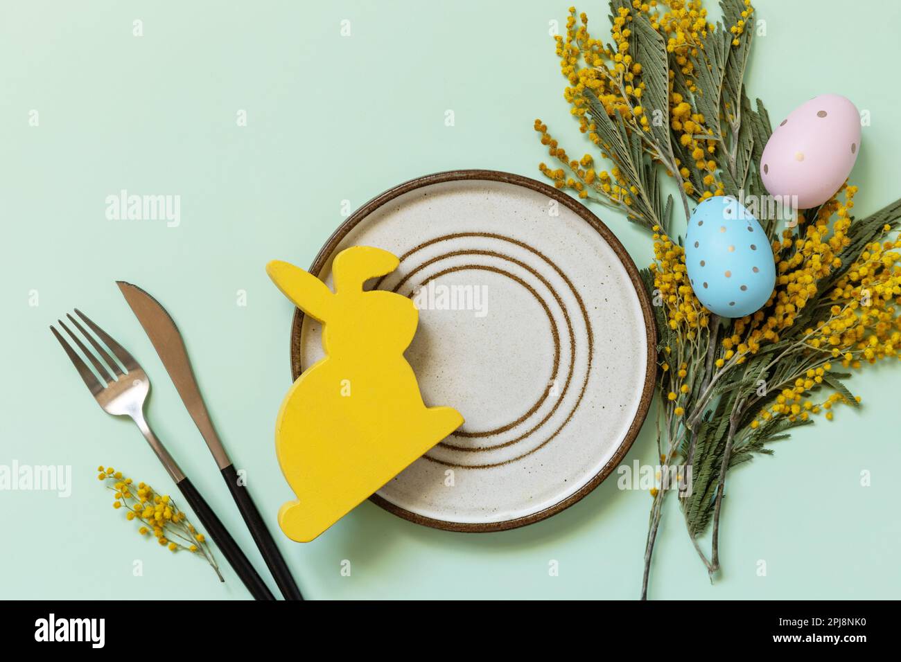 Réglage de la table de Pâques. Assiette avec œufs de pâques et mimosa sur fond vert pastel. Happy Easter Holiday concept pour les restaurants. Vue de dessus. Banque D'Images