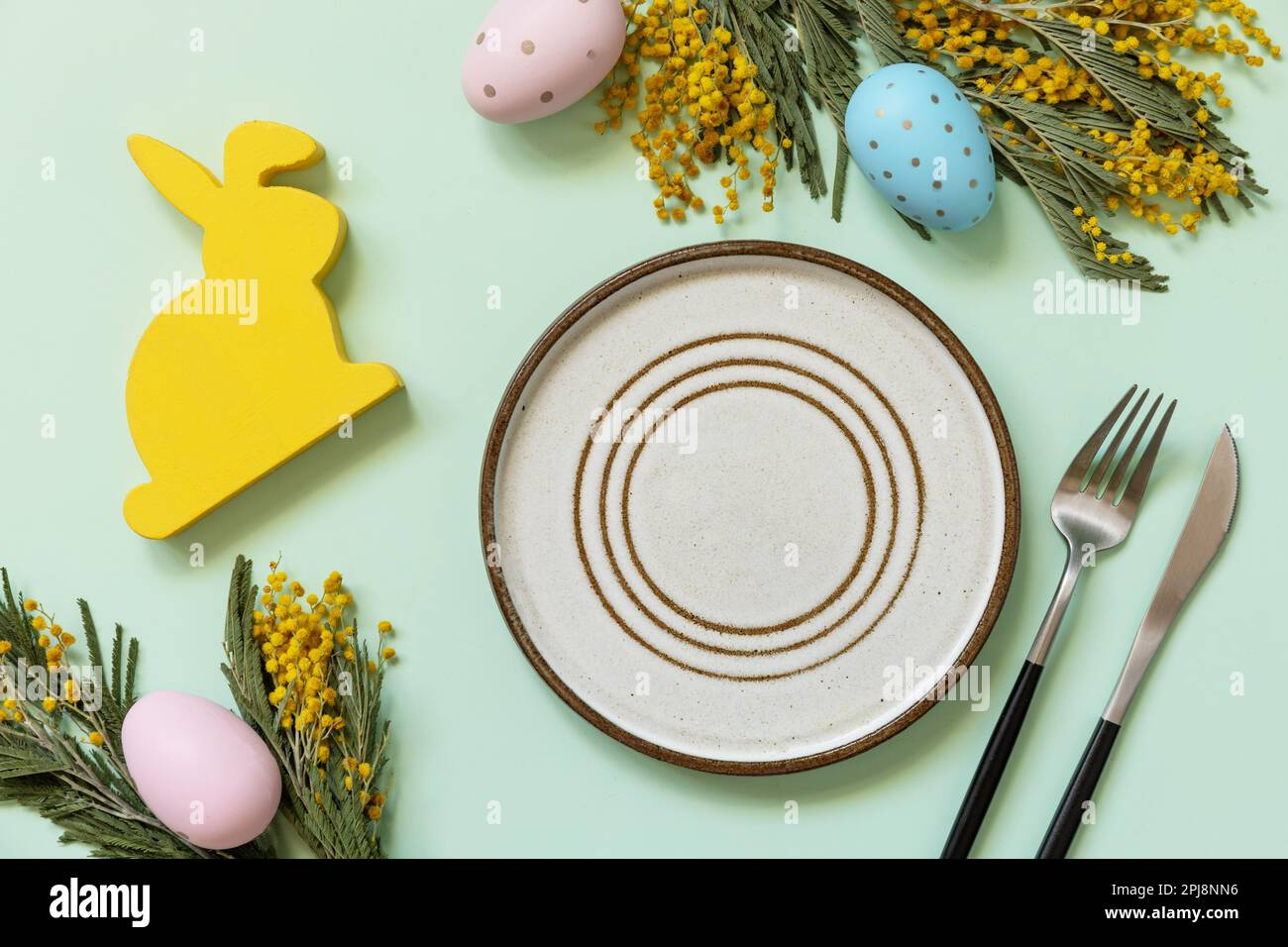 Réglage de la table de Pâques. Assiette avec œufs de pâques et mimosa sur fond vert pastel. Happy Easter Holiday concept pour les restaurants. Vue de dessus. Banque D'Images