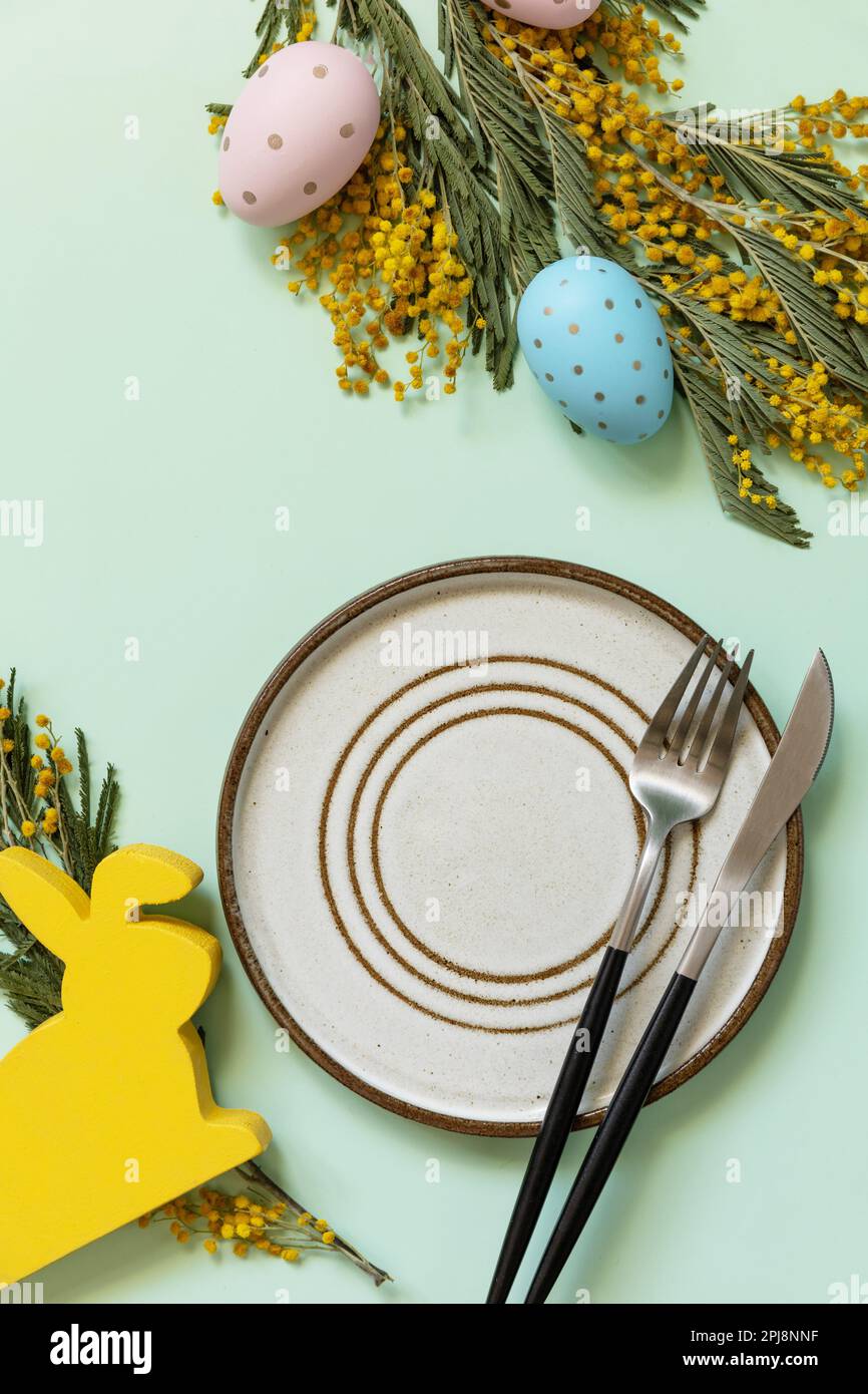 Réglage de la table de Pâques. Assiette avec œufs de pâques et mimosa sur fond vert pastel. Happy Easter Holiday concept pour les restaurants. Vue de dessus. C Banque D'Images
