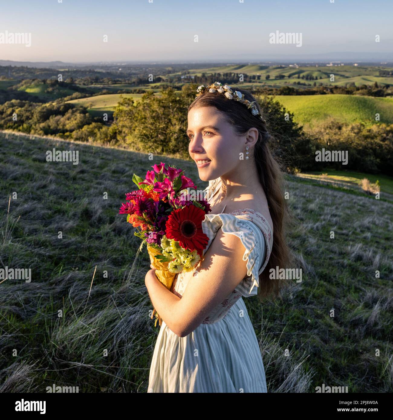 Jeune femme en robe de chalet et corsage en lacé marcher à Palo Alto Hills Voir une vue | bouquet de fleurs | serre-tête à fleurs Banque D'Images