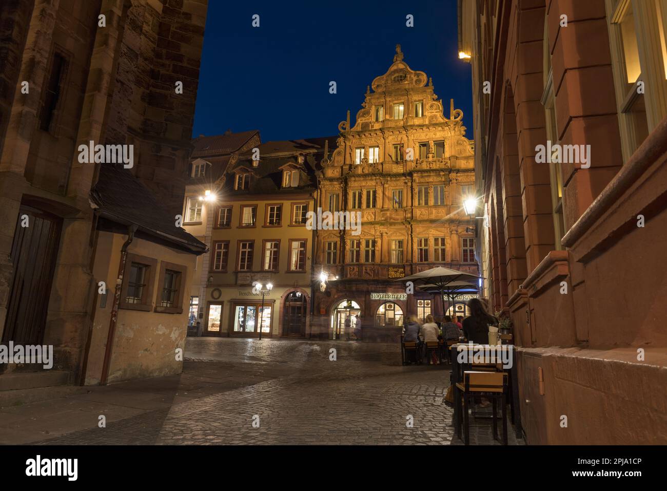 Les gens dans le café ou le bar par l'historique 16e siècle médiéval Hôtel zum Ritter dans Hauptstrasse dans la vieille ville de Fischmarkt la nuit ou au crépuscule. Heidelberg. Banque D'Images