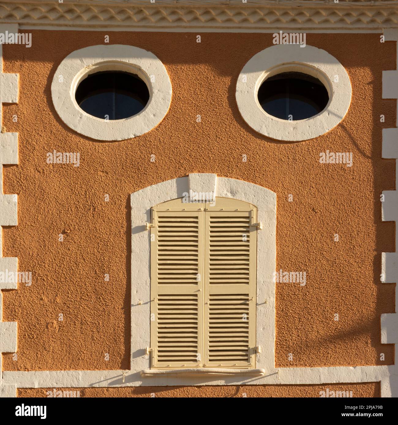 Détail architectural unique d'une façade de bâtiment avec fenêtres circulaires et porte à volets dans un endroit ensoleillé Banque D'Images