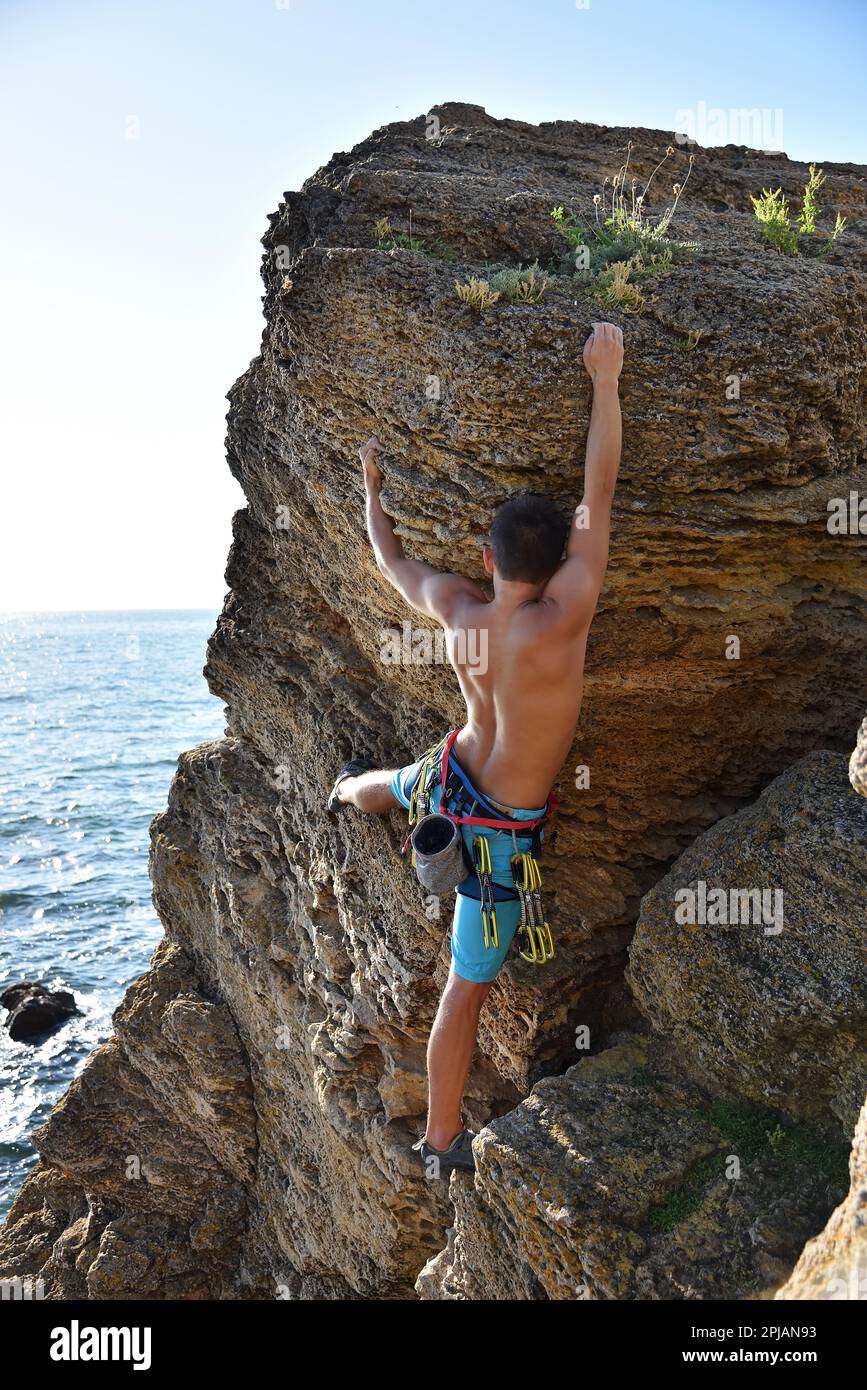 Jeune homme grimpant sur un rocher avec la mer sur le fond Banque D'Images