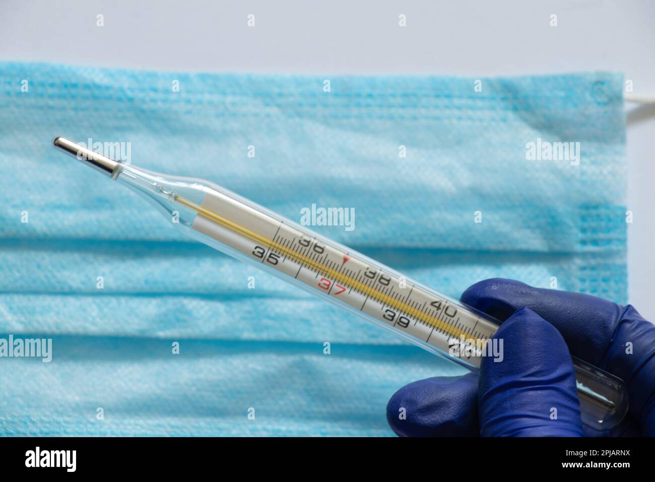 Thermomètre en verre et main dans un gant bleu sur le fond du masque Medetsyn Banque D'Images