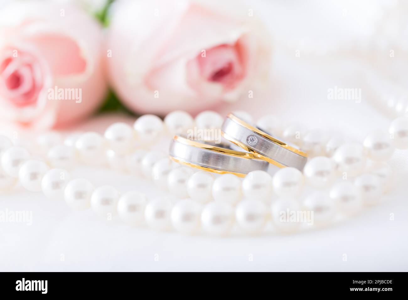 Anneaux de mariage modernes avec collier de perles avec roses roses roses en arrière-plan, doux foyer Banque D'Images
