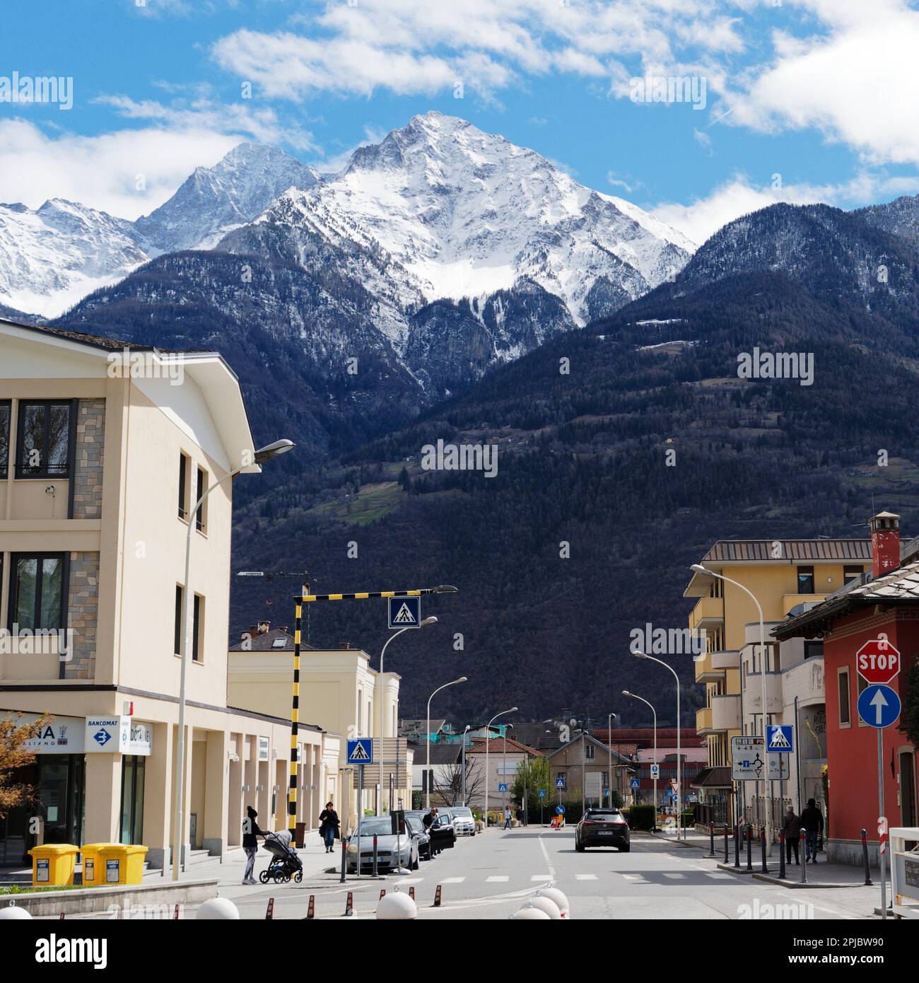 Les montagnes enneigées surplombent la ville d'Aoste tandis que quelqu'un pousse une poussette vers une traversée de zèbre. Aoste Vally, Italie Banque D'Images