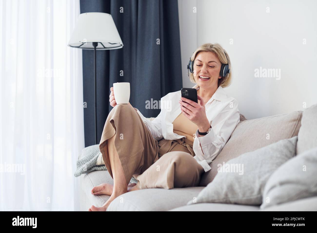 Femme d'âge moyen dans des vêtements élégants est à la maison utilise le téléphone Banque D'Images