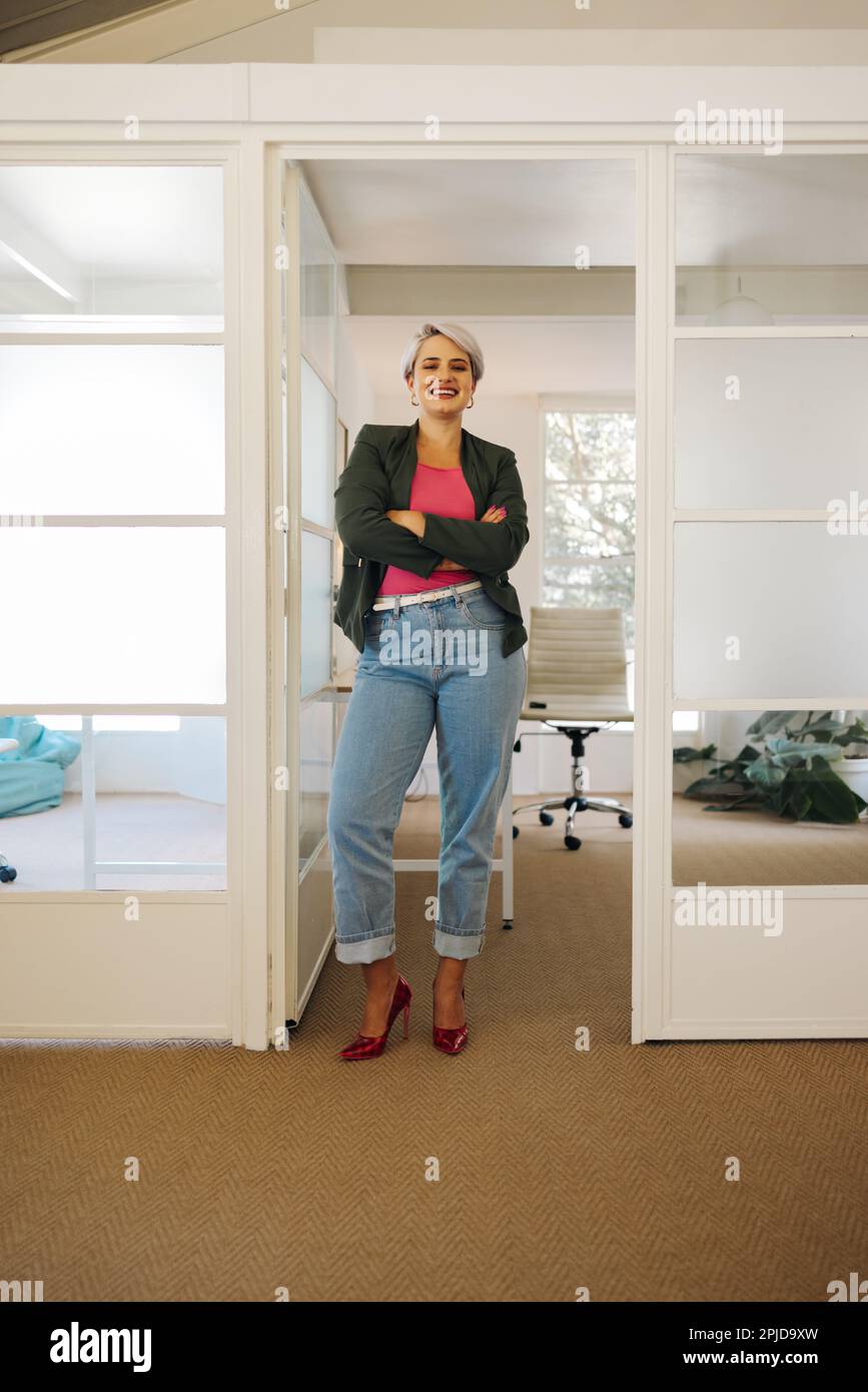 Femme d'affaires moderne souriant à la caméra tout en se tenant devant son bureau. Femme entrepreneure prospère travaillant dans un milieu de travail créatif. Banque D'Images