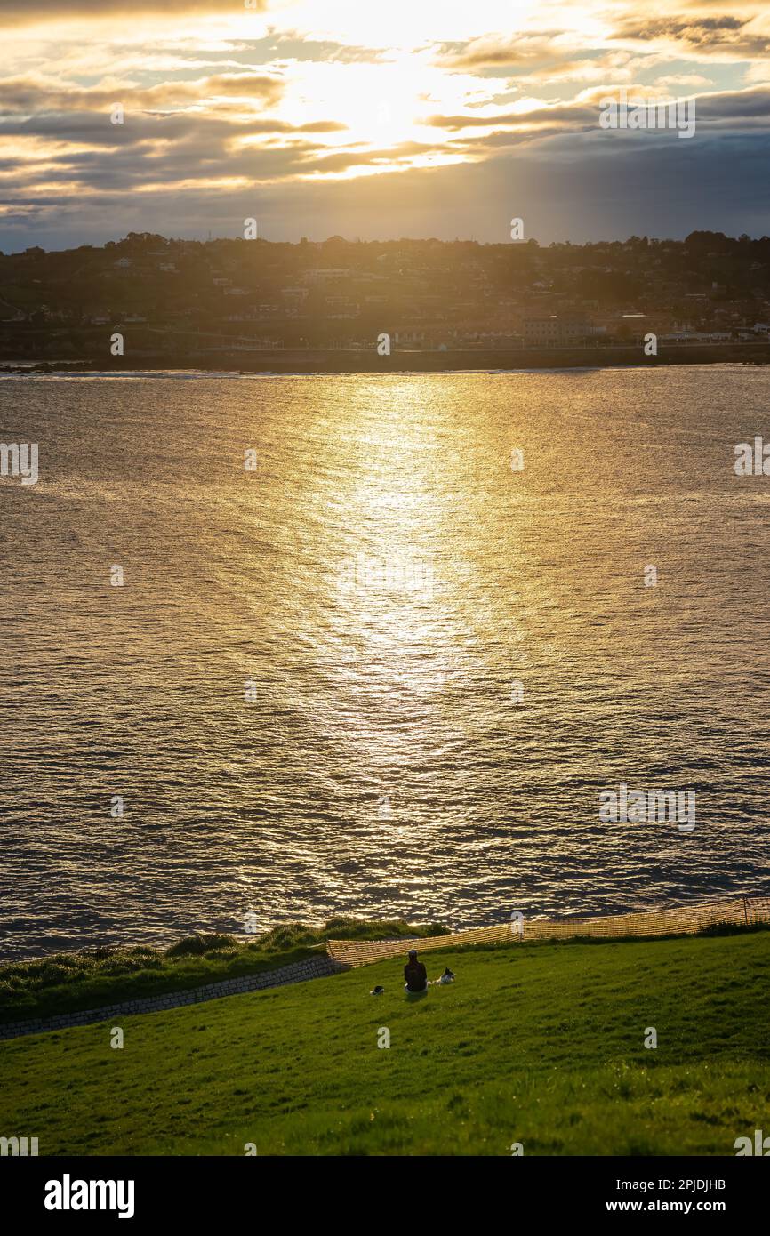 Beau lever de soleil au-dessus de la ville de Gijon avec des reflets dorés sur les vagues de la mer lors d'une journée calme et sereine. Banque D'Images