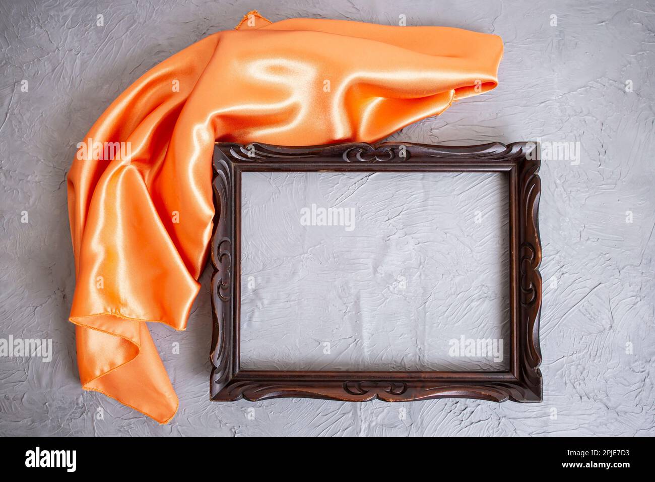Cadre en bois vide dévoilé par un drapé de satin orange, sur texture de ciment gris Banque D'Images
