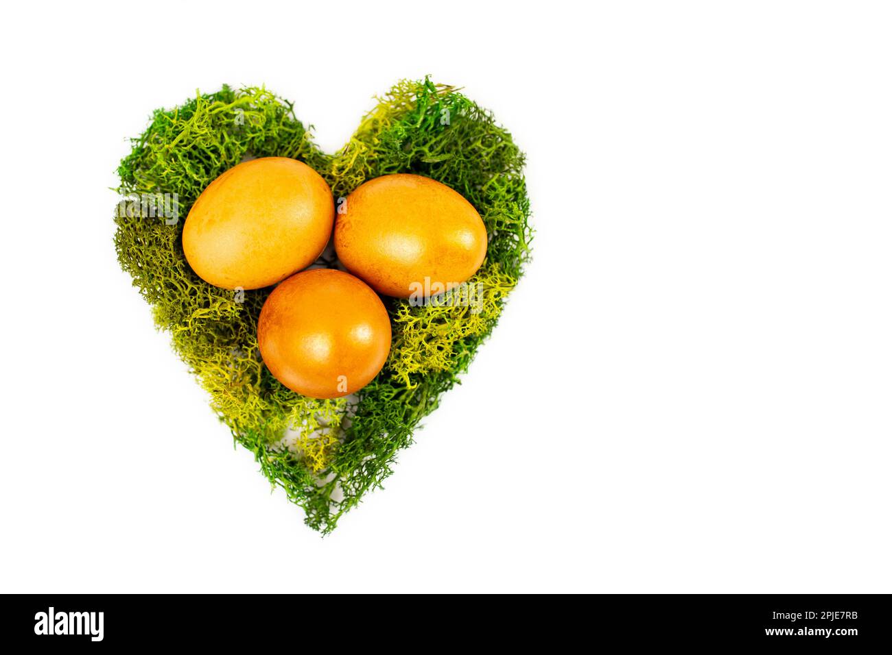 Trois œufs d'or dans un nid en forme de coeur fait de mousse verte isolée sur fond blanc Banque D'Images