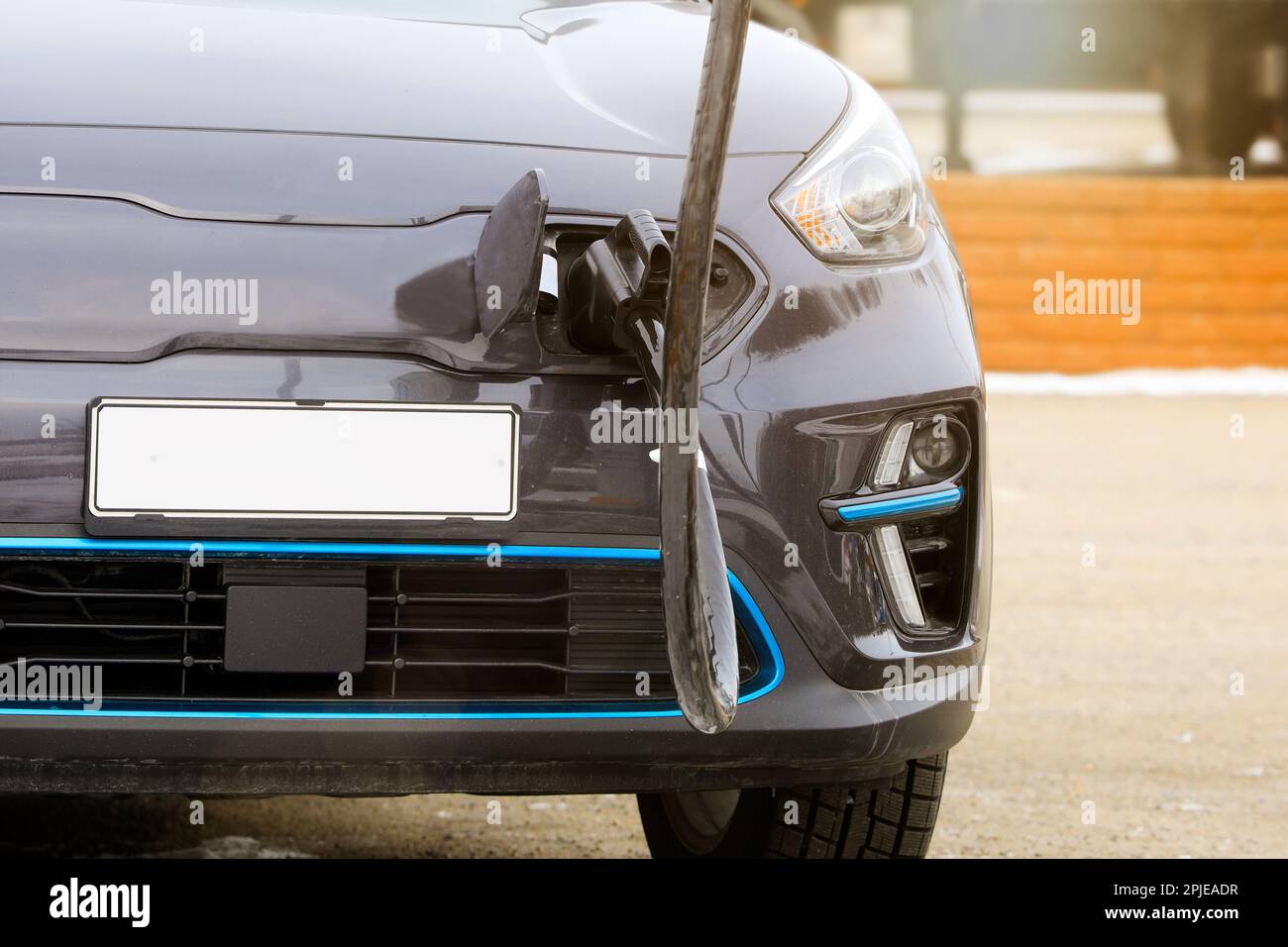 Voiture électrique branchée à la station de charge pour recharger la batterie, détail, vue avant, lumière du soleil ajoutée. Personne, logos, etc. Supprimés. Banque D'Images