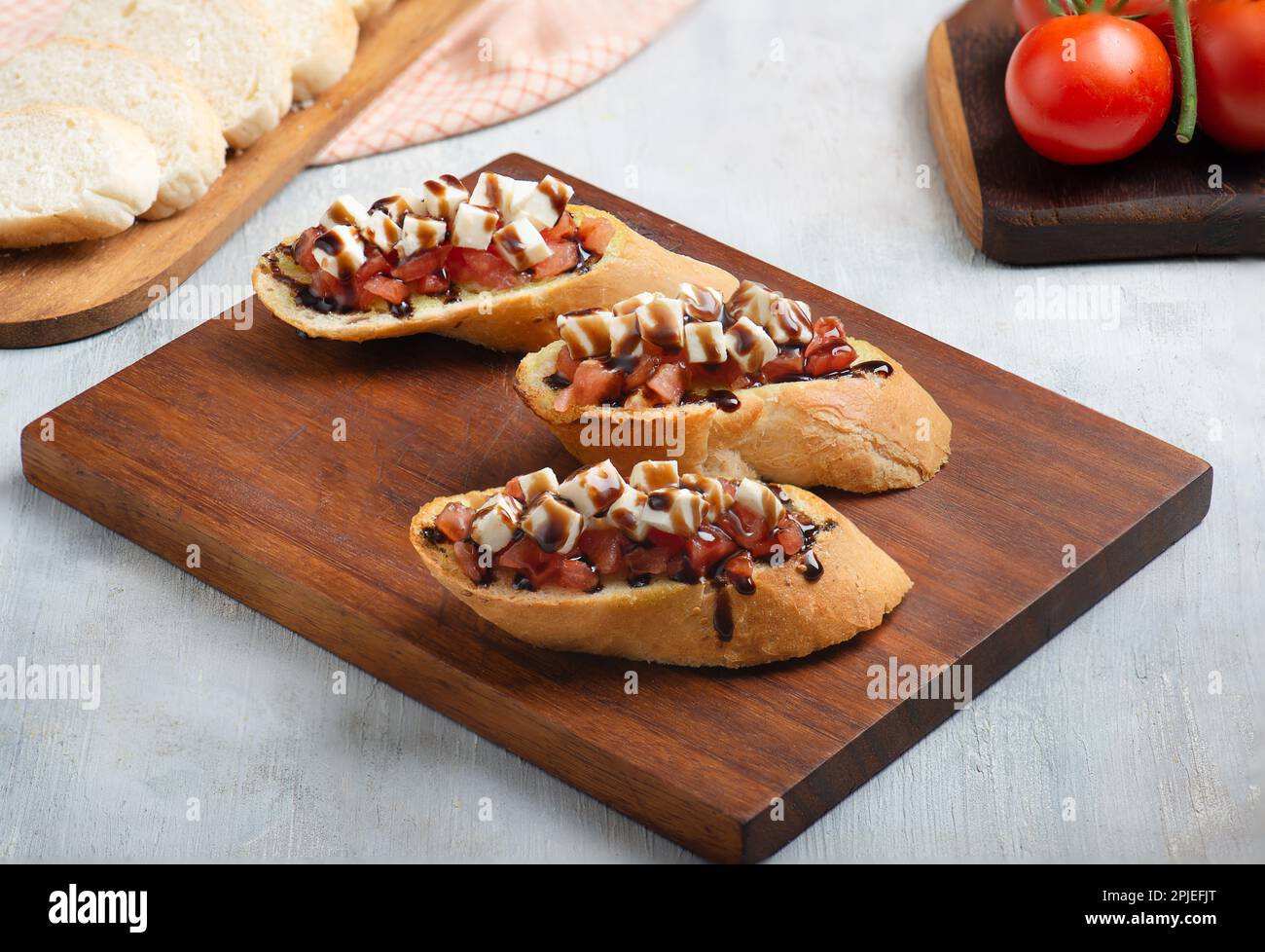 Trois morceaux de bruschetta à la tomate, à la mozzarella et au vinaigre balsamique sur un plateau de service en bois Banque D'Images