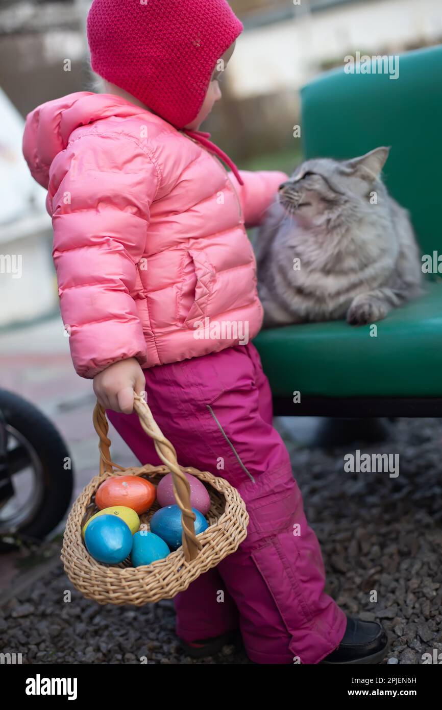 Une petite fille avec un panier d'oeufs de Pâques se déplace un chat domestique dans la cour . Style de vie. Célébration de Pâques Banque D'Images