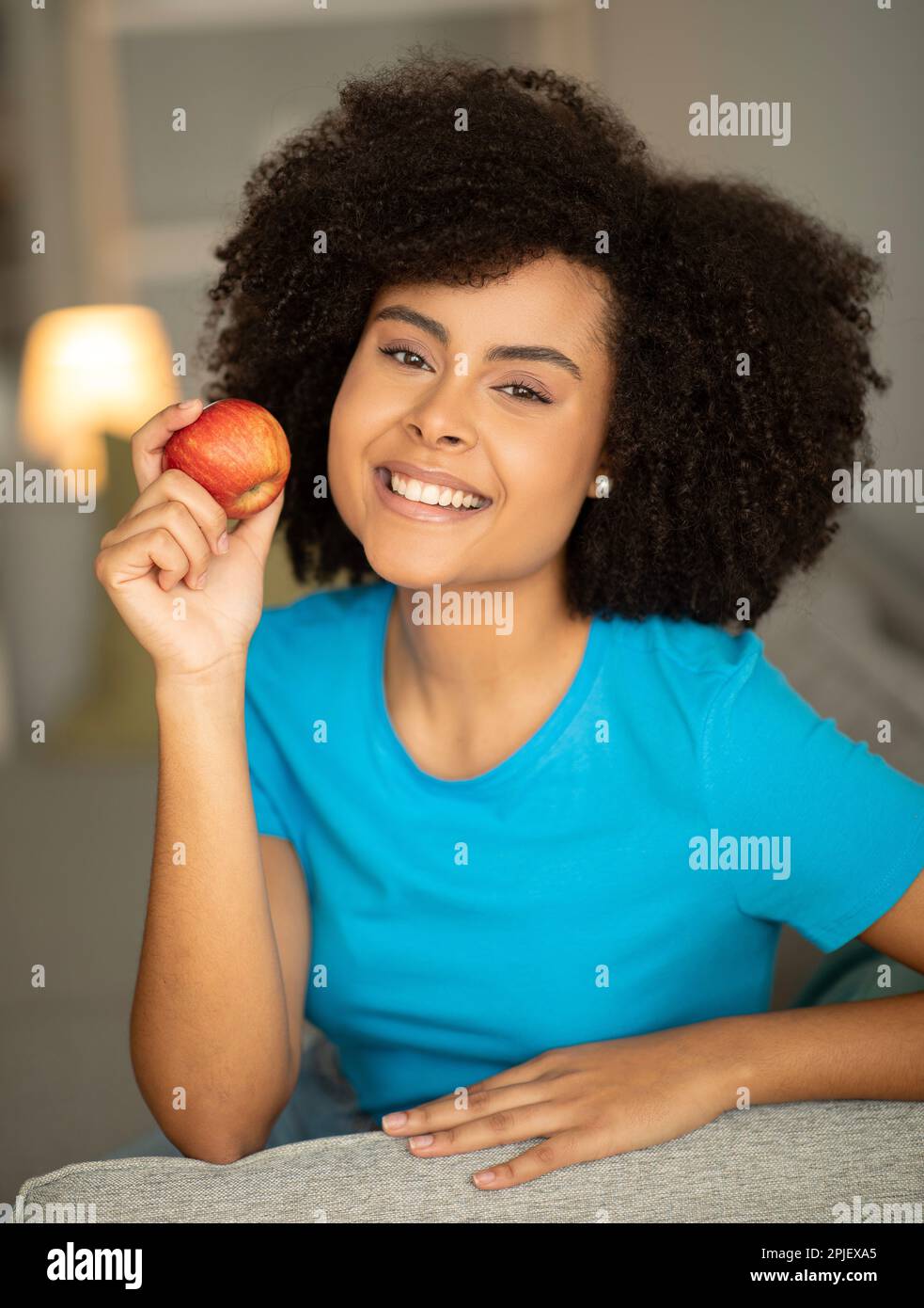 Joyeuse femme maurique afro-américaine millénaire, profitez de la pomme sur le canapé dans le salon intérieur, gros plan Banque D'Images