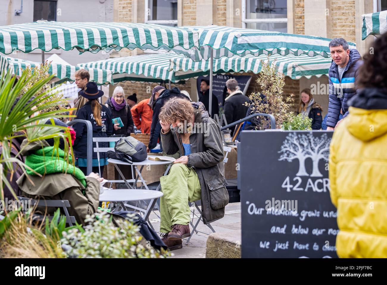 Un jeune homme à poil long et à barbe s'est assis à lire le livre au café en plein air du marché du dimanche de Frome, Somerset, Royaume-Uni, le 2 avril 2023 Banque D'Images