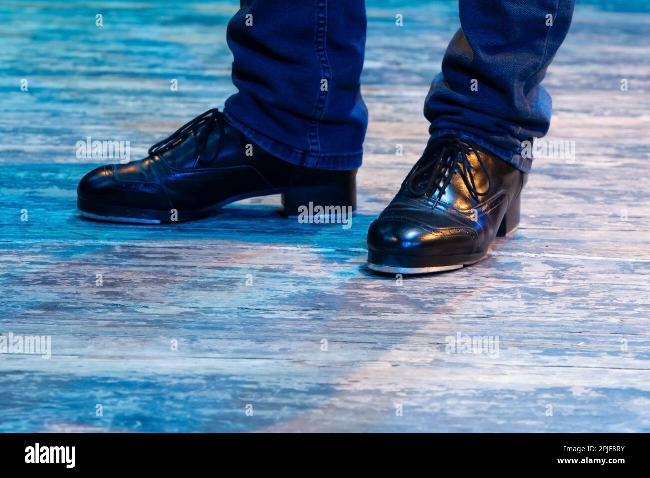 Les jambes des hommes en mouvement dans le pantalon de scène avec des rayures et des chaussures en cuir pour la danse irlandaise sur le sol. Chaussures de travail noires pour danser le robinet avec réflexion Banque D'Images