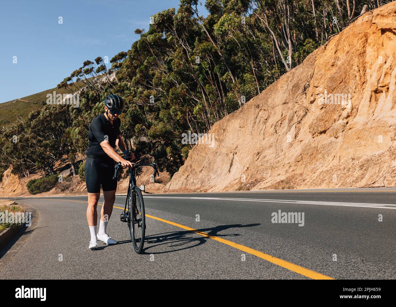 Cycliste de sexe masculin inspectant son vélo tout en se tenant sur une  route vide Photo Stock - Alamy