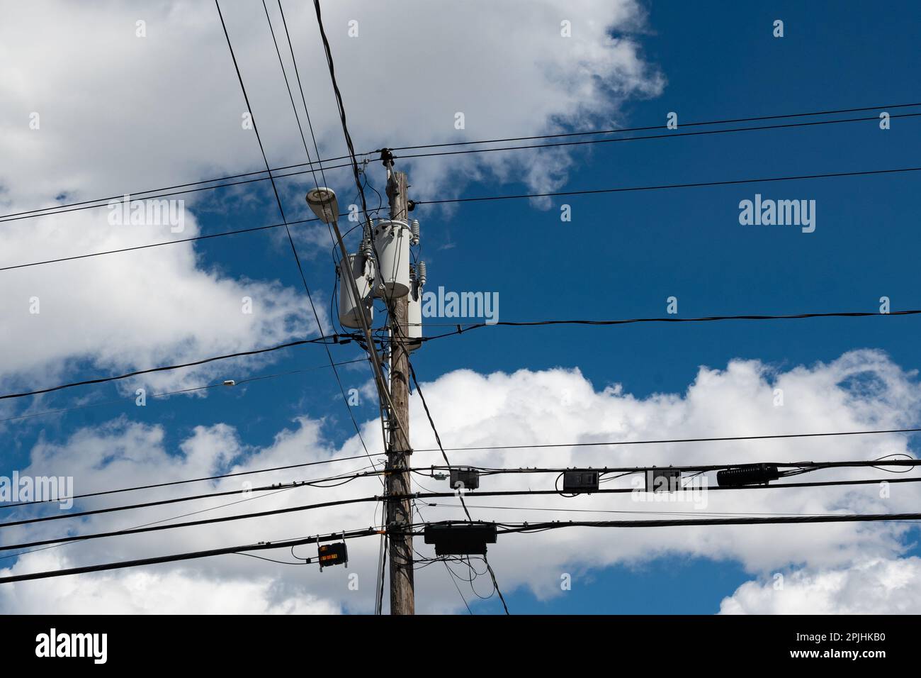 Un poteau utilitaire avec transformateurs et de nombreux câbles et boîtes de communication, lumière de rue LED avec un ciel bleu et un fond de nuage blanc Banque D'Images
