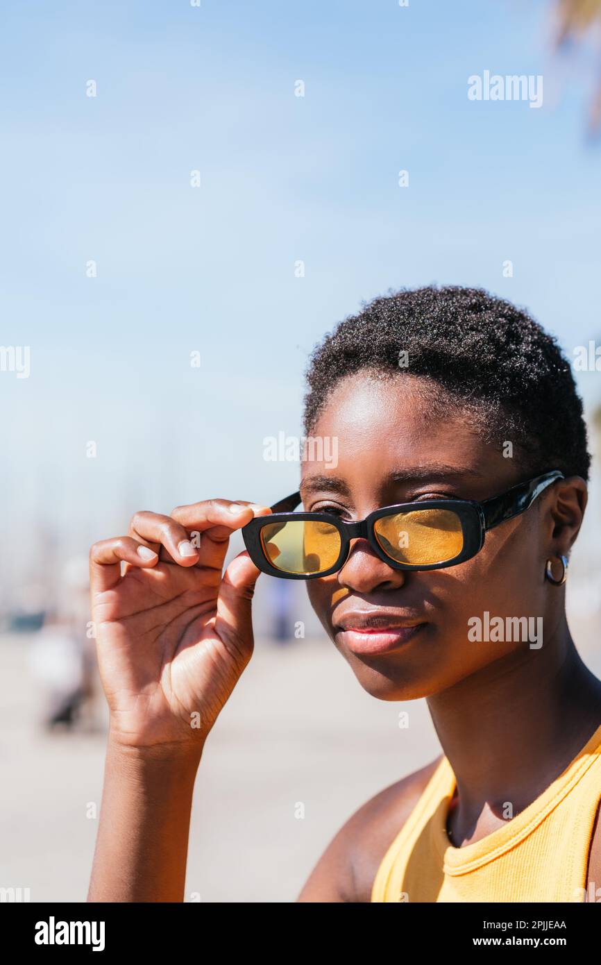 portrait vertical d'une femme africaine attrayante en retirant des lunettes de soleil jaunes à la mode Banque D'Images