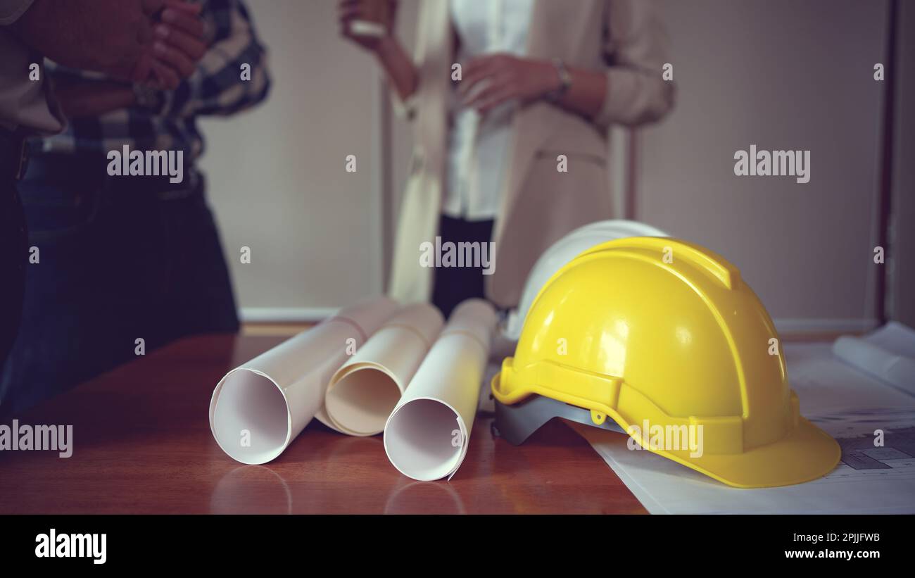 Vue rapprochée de la table de travail de l'ingénieur avec casque de sécurité et plan de travail sur le bureau dans la salle de bureau. Banque D'Images