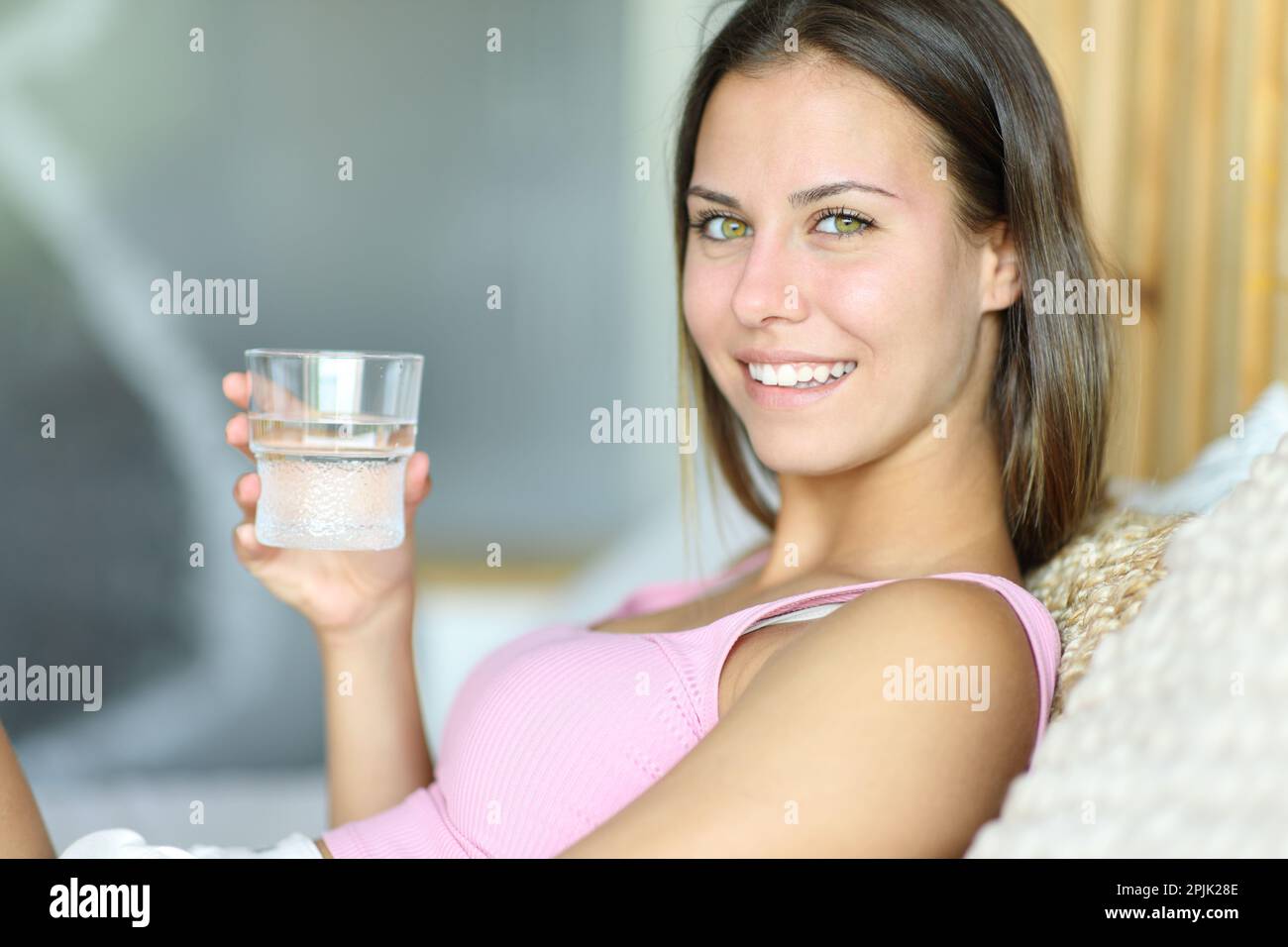 L'adolescent tenant un verre d'eau regarde la caméra dans un lit à la maison Banque D'Images