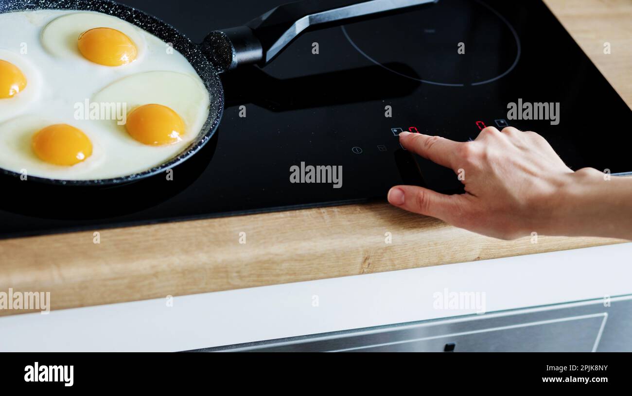 une femme cuisine le petit déjeuner sur une poêle. des femelles cuisent des œufs sur une cuisinière à induction. Une fille prépare le repas dans une cuisine moderne Banque D'Images