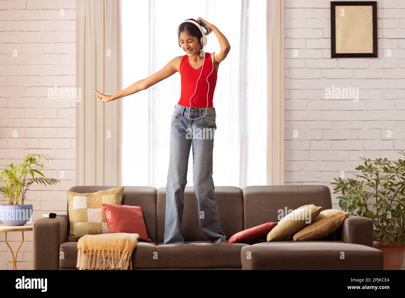 Une fille écoute de la musique dans un casque et danse sur un canapé dans le salon Banque D'Images