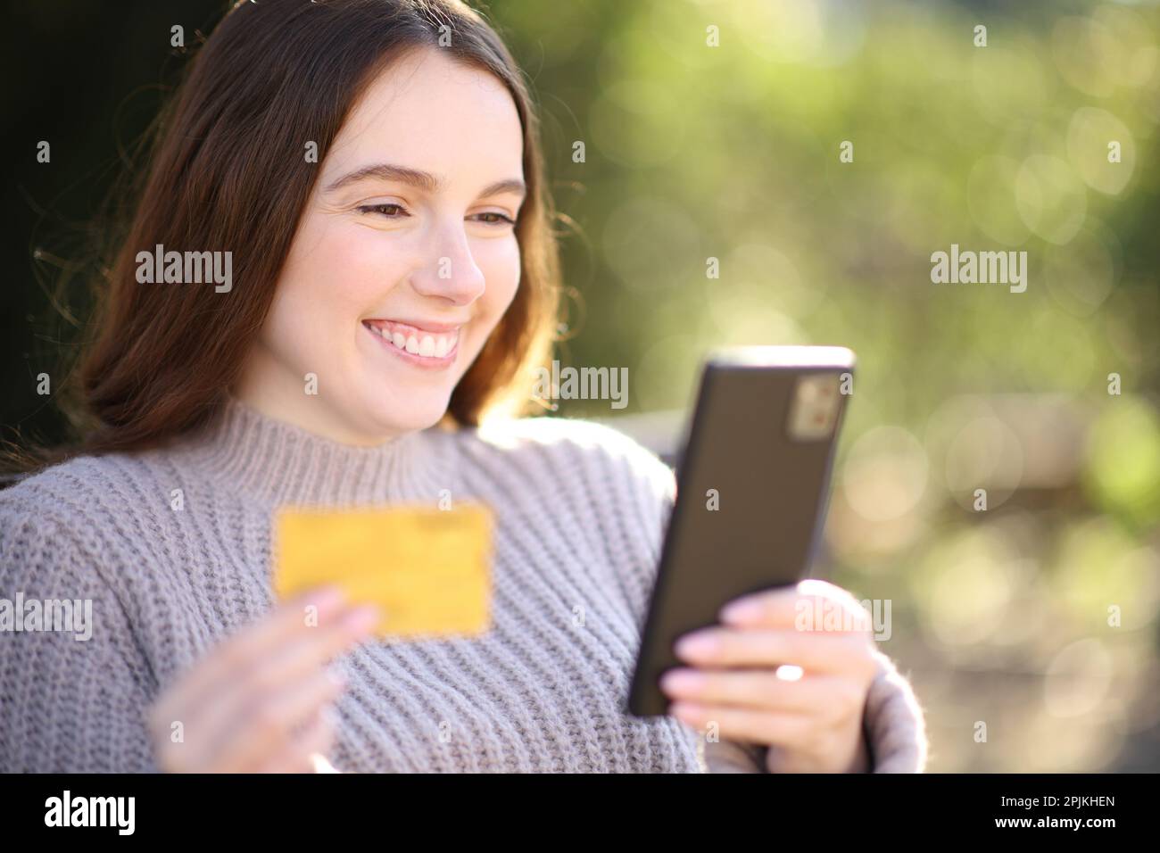 Bonne femme achetant en ligne avec téléphone et carte de crédit dans un parc Banque D'Images