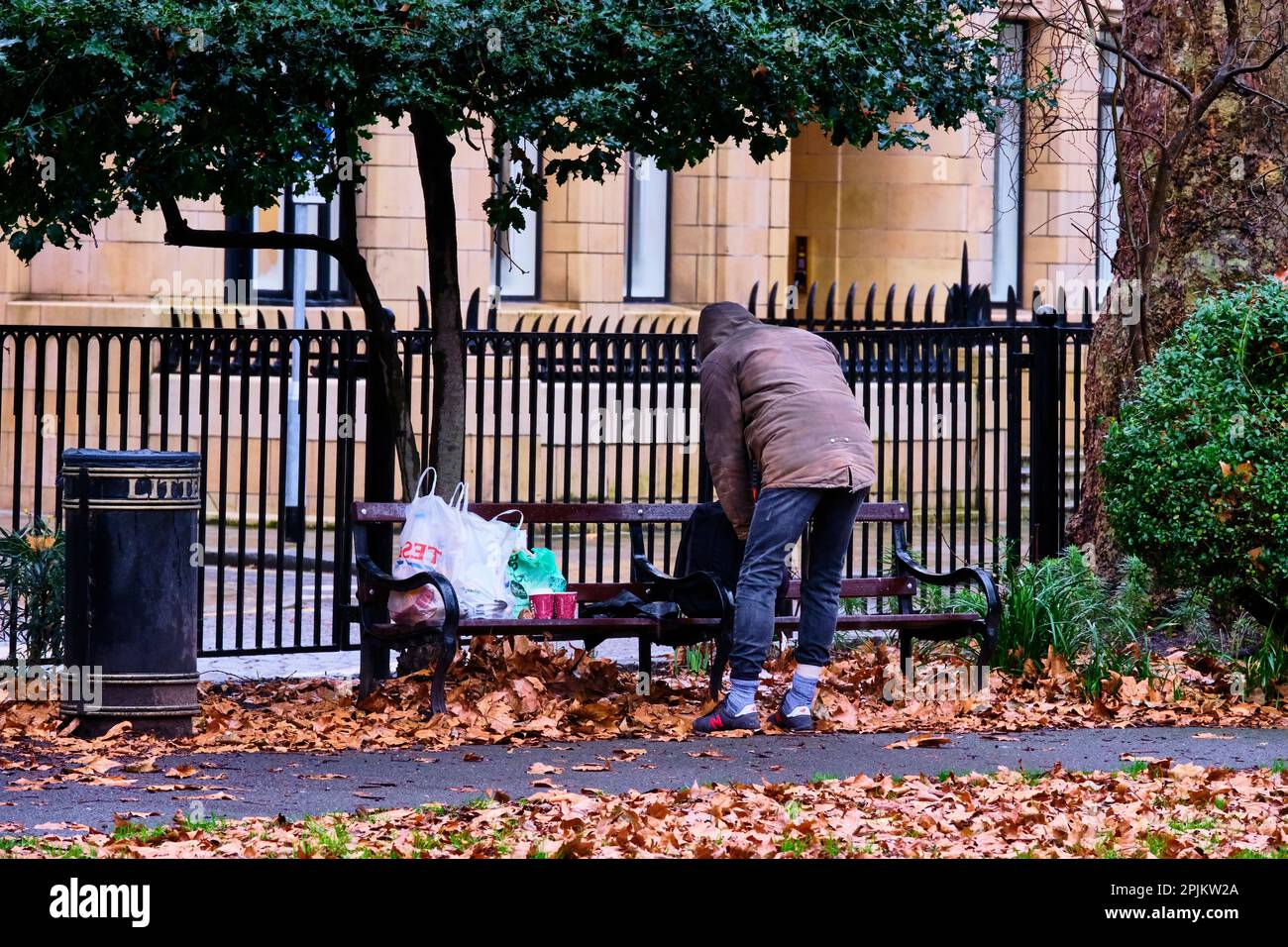 Guy sans-abri ramasse ses affaires sur un banc de parc. Banque D'Images