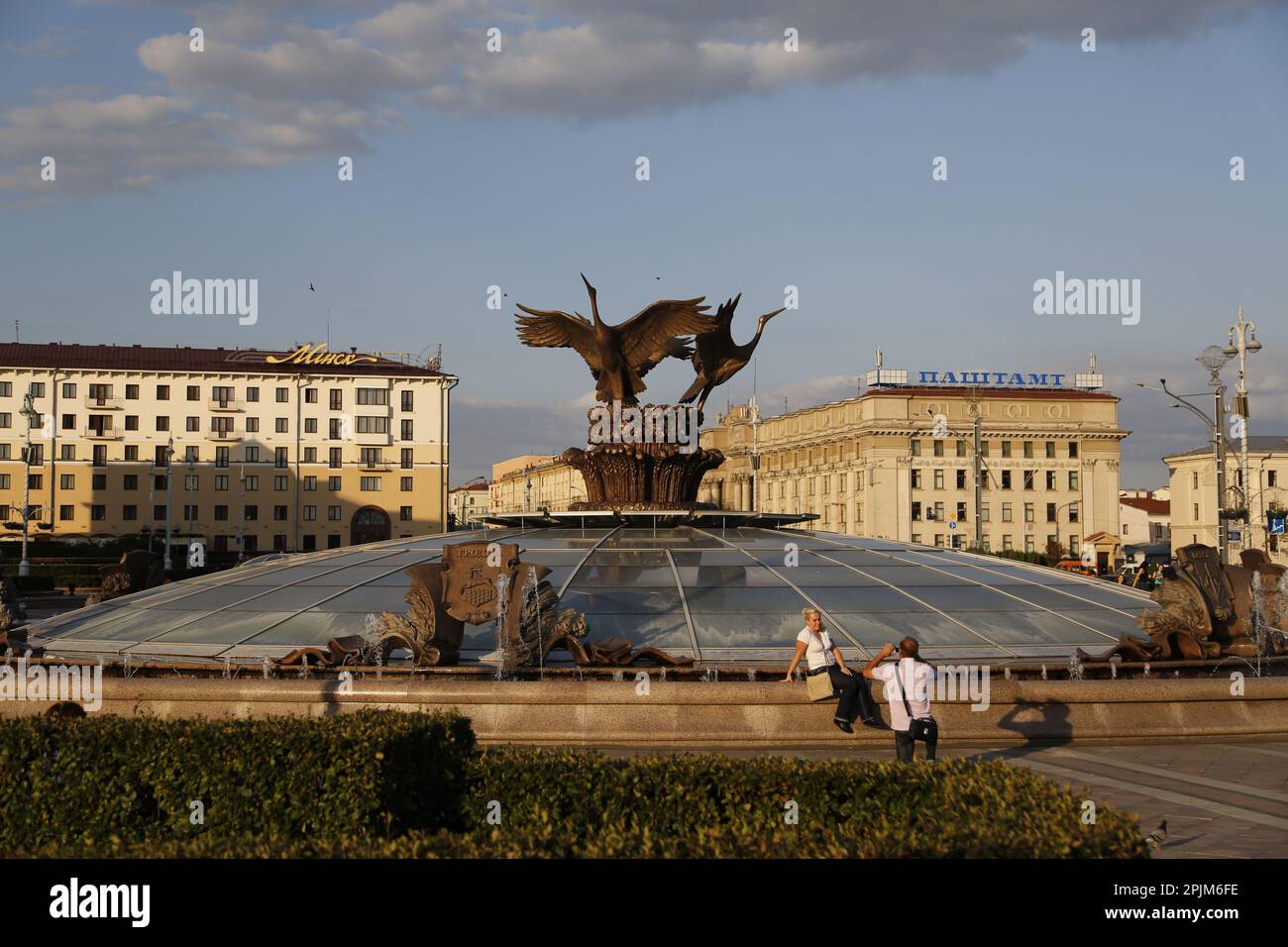 Un couple prend des photos près de la statue de Stork sur la coupole de la place de l'indépendance (ancienne place Lénine) à Minsk, en Biélorussie; bureau de poste principal en arrière-plan Banque D'Images