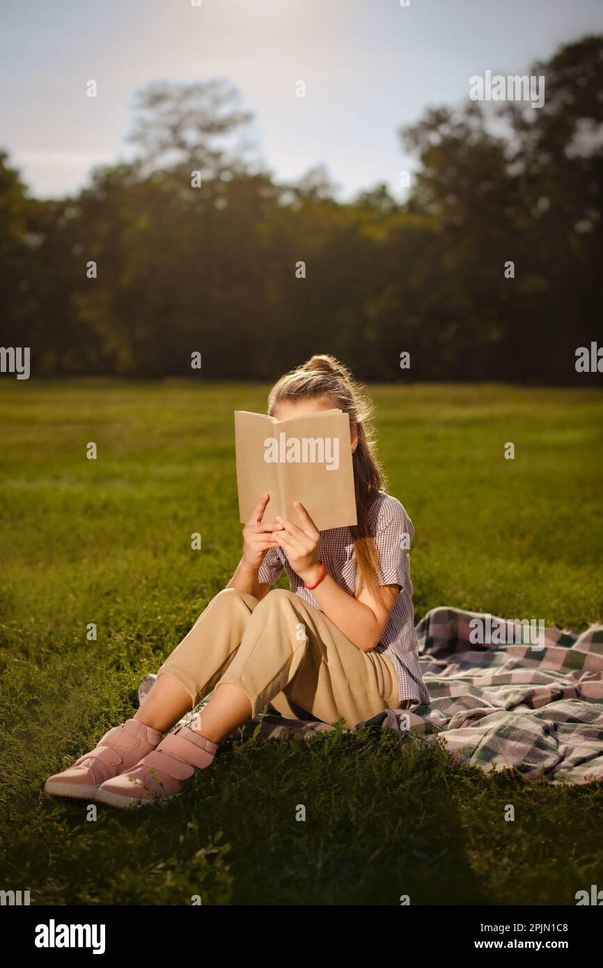 enfant fille tenant un modèle de couverture de livre écologique et cache son visage derrière le livre assis à l'extérieur dans le parc Banque D'Images