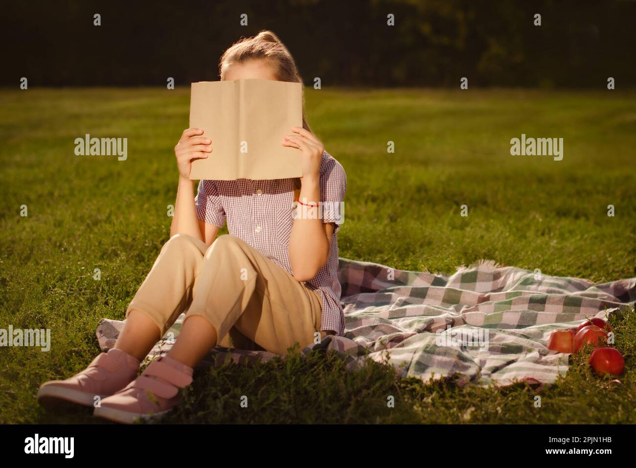 adolescente tenant le livre dans les mains et face étroite avec ordinateur portable assis à l'extérieur dans le parc Banque D'Images