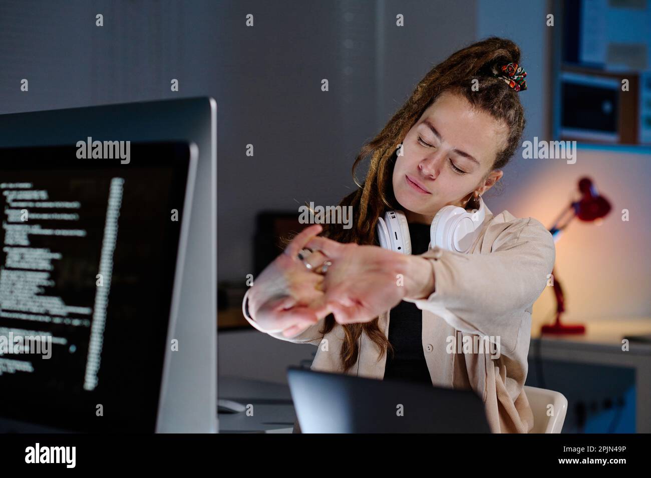 Jeune femme fatiguée responsable DE l'ASSISTANCE INFORMATIQUE avec des dreadlocks qui étirent les bras devant elle tout en ayant une minute de détente sur le lieu de travail Banque D'Images