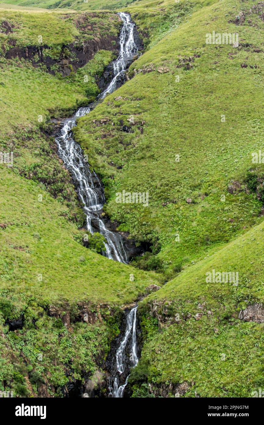 Les chutes d'eau de Mahai, vues de loin, s'écoulent en cascade sur une pente escarpée couverte d'herbe des montagnes du Drakensberg en Afrique du Sud. Banque D'Images