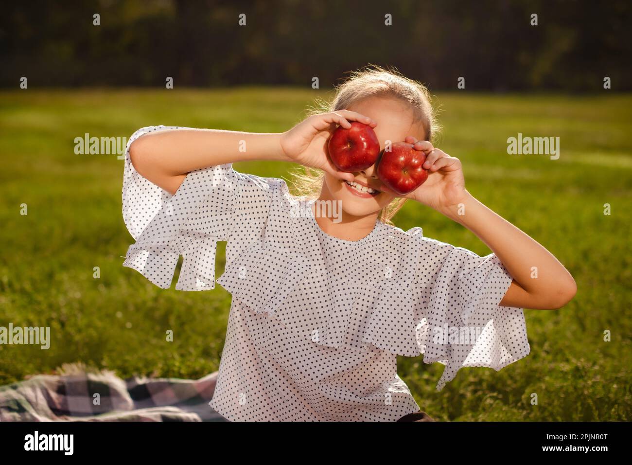 une jeune fille s'amuse avec des pommes sur l'herbe verte dans le parc. pause à l'école. une fille cache le visage avec des pommes fraîches rouges Banque D'Images