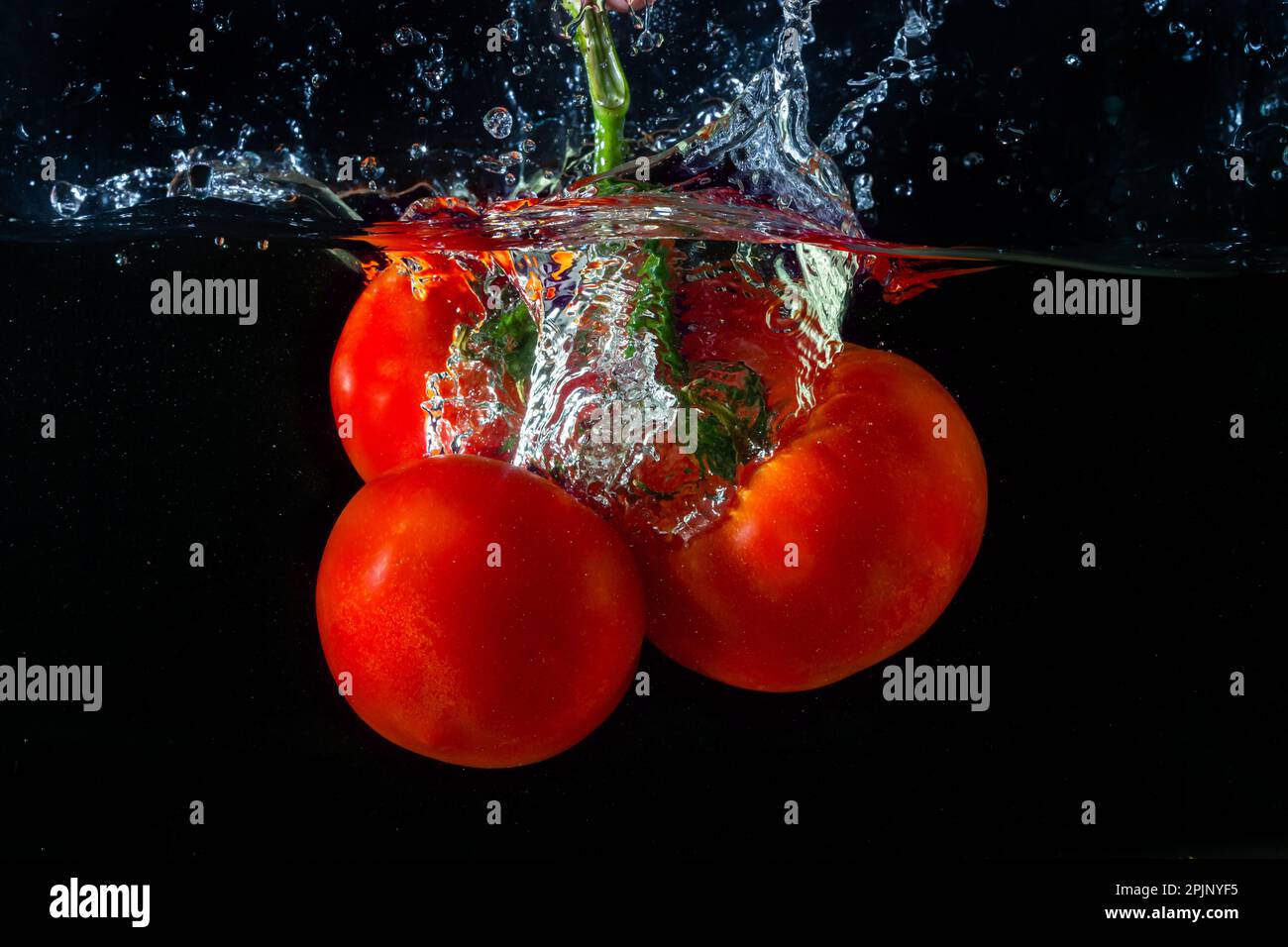 Tomate rouge fraîche tombant dans l'eau avec des éclaboussures d'eau et des bulles d'air isolées sur fond noir. Banque D'Images