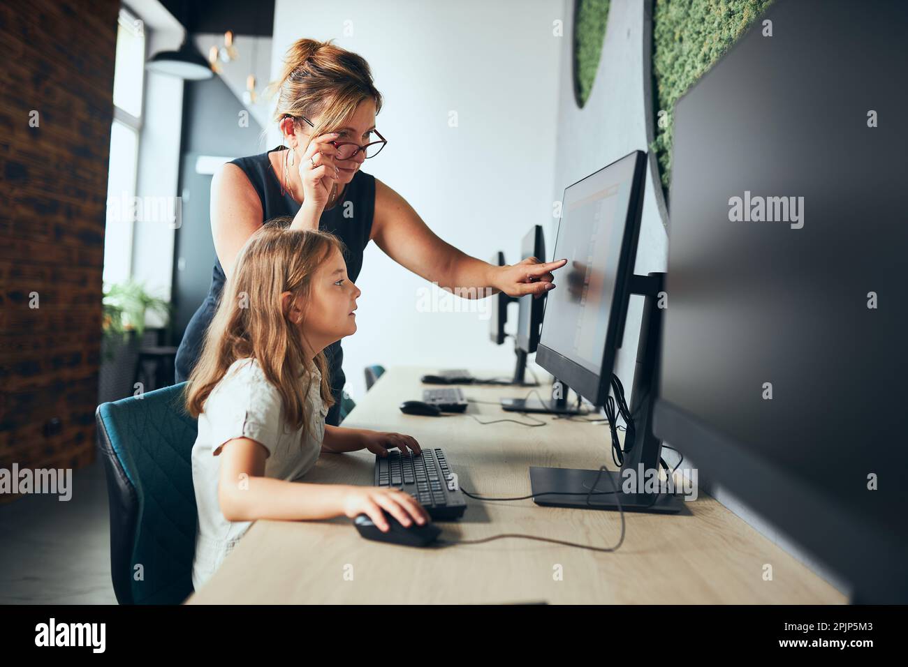 Cours d'informatique à l'école. Enseignant aidant une écolière pendant la classe à l'école primaire. Ordinateur d'apprentissage d'enfant sur la leçon élémentaire d'informatique. T Banque D'Images