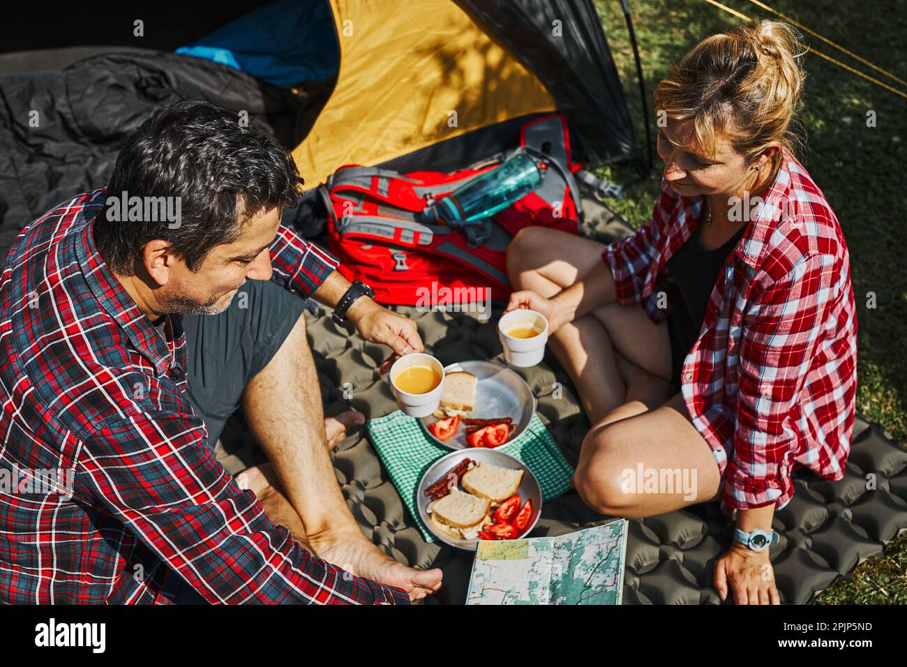 Couple prenant le petit déjeuner et planifiant leur journée assise par tente au camping. Les gens passent activement des vacances d'été près de la nature en plein air. Concept Banque D'Images