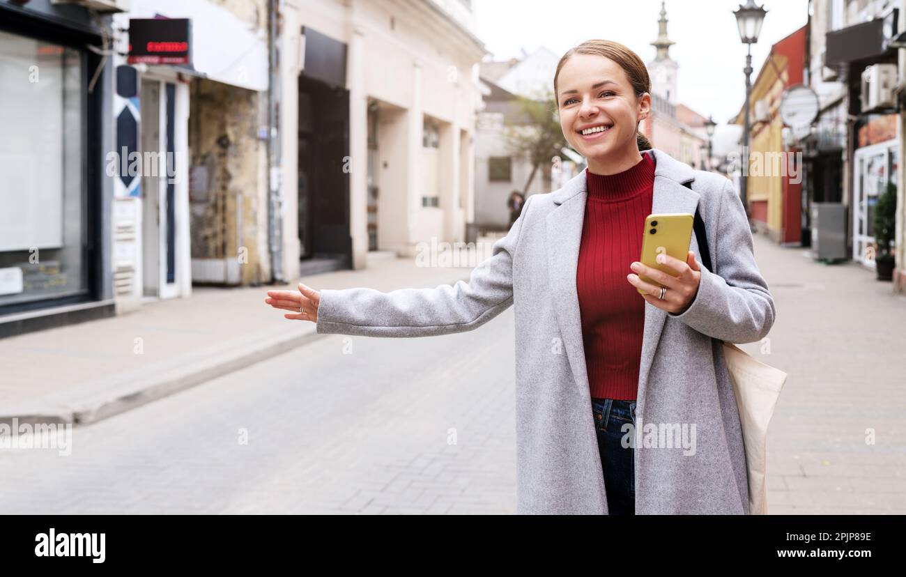 Femme élégante portant un manteau debout dans la rue et en train de héler un taxi. Banque D'Images