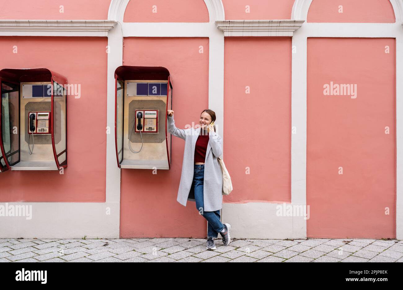 Femme debout à côté de la rue de téléphone public et parlant sur le téléphone mobile. Banque D'Images