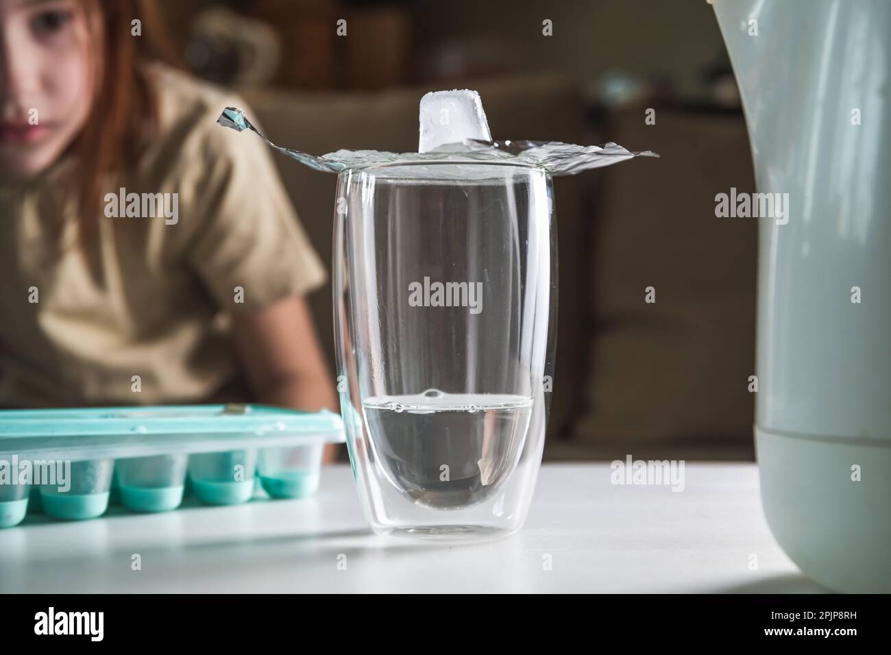 une écolière réalise une expérience avec de l'eau chaude et de la glace. expérience de l'obtention de nuages dans un verre. vapeur, condensation, devoirs, études Banque D'Images