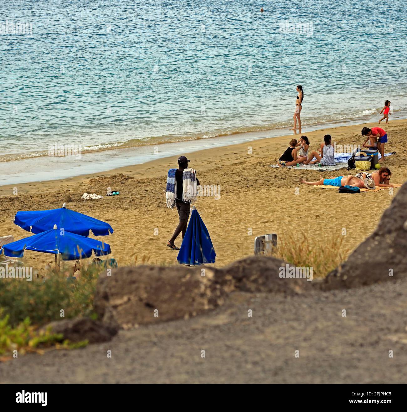 Noir, homme vendeur de serviettes montrant ses articles aux vacanciers, Playa Blanca Beach. Février 2023 Banque D'Images