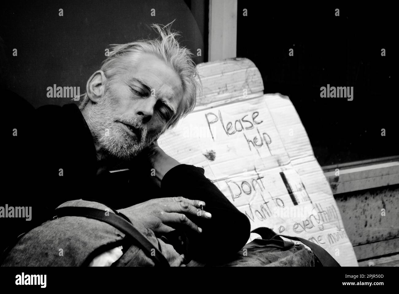 Un homme sans domicile tente de dormir dans une porte et a soutenu un panneau sur un morceau de carton demandant aux passants de l'aide. Banque D'Images