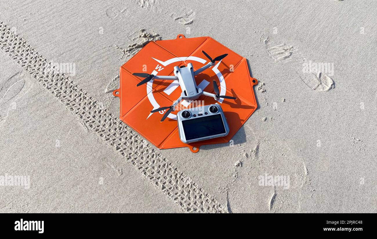 Un drone avec son contrôleur sur un décollage orange et un débarcadère reposant sur le sable à une plage. Banque D'Images