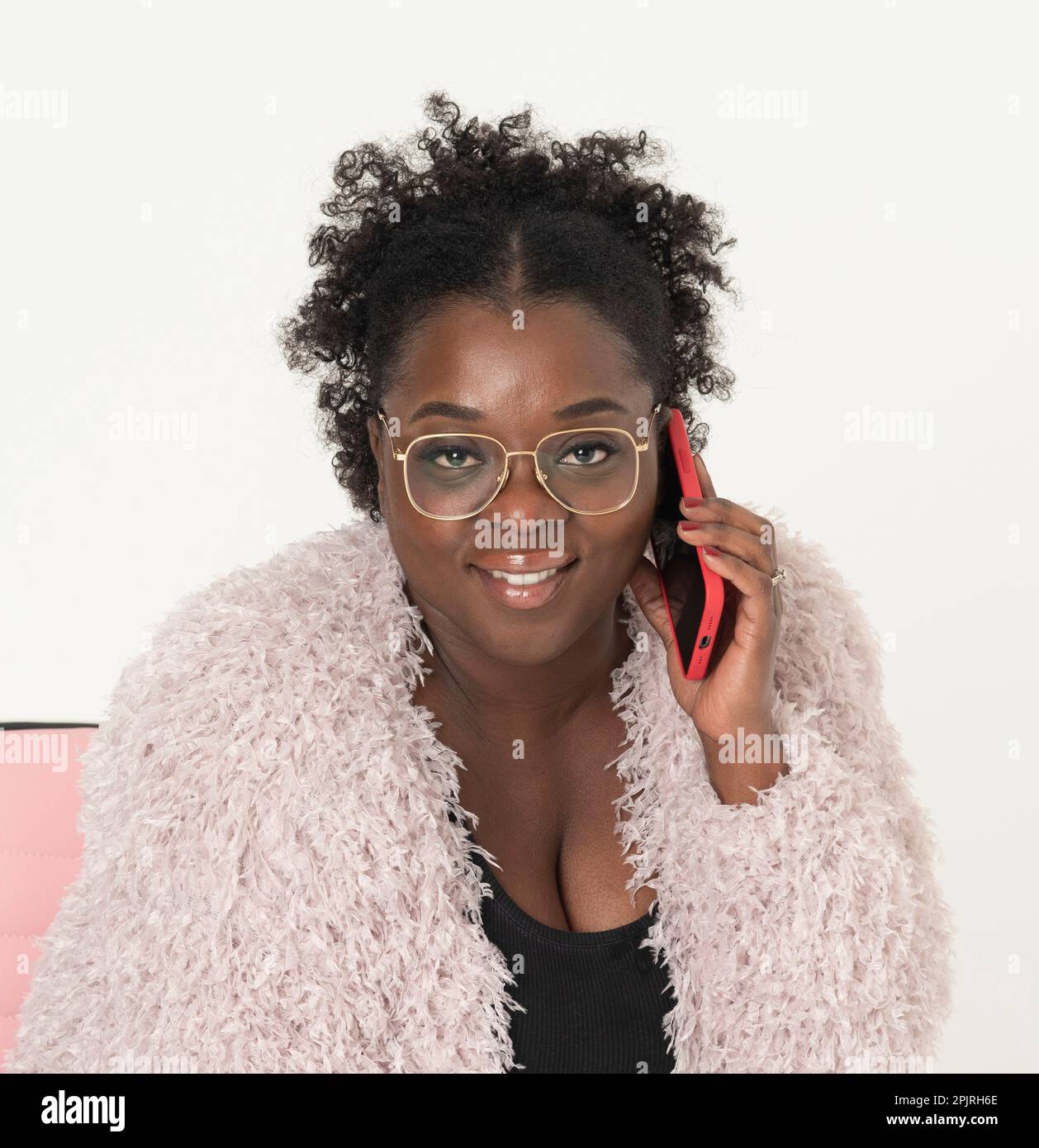 Angleterre, Royaume-Uni. 2022. Portrait d'une femme africaine attrayante utilisant un téléphone portable dans un étui en plastique rouge. Banque D'Images