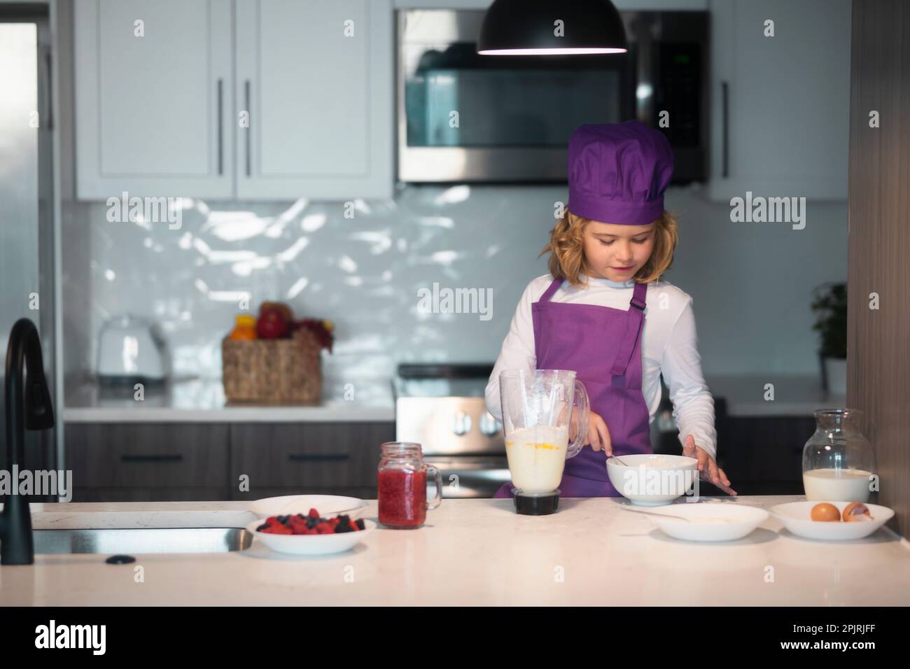 Enfant de 7-8 ans en chapeau de chef et tablier. Les enfants préparent la pâte, cuisent des biscuits dans la cuisine Banque D'Images