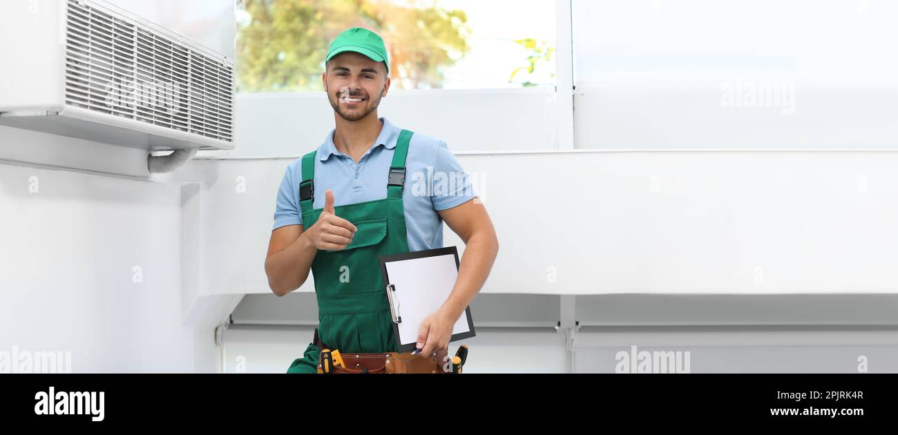 Technicien professionnel avec presse-papiers à proximité du climatiseur moderne à l'intérieur, espace pour le texte. Bannière Banque D'Images